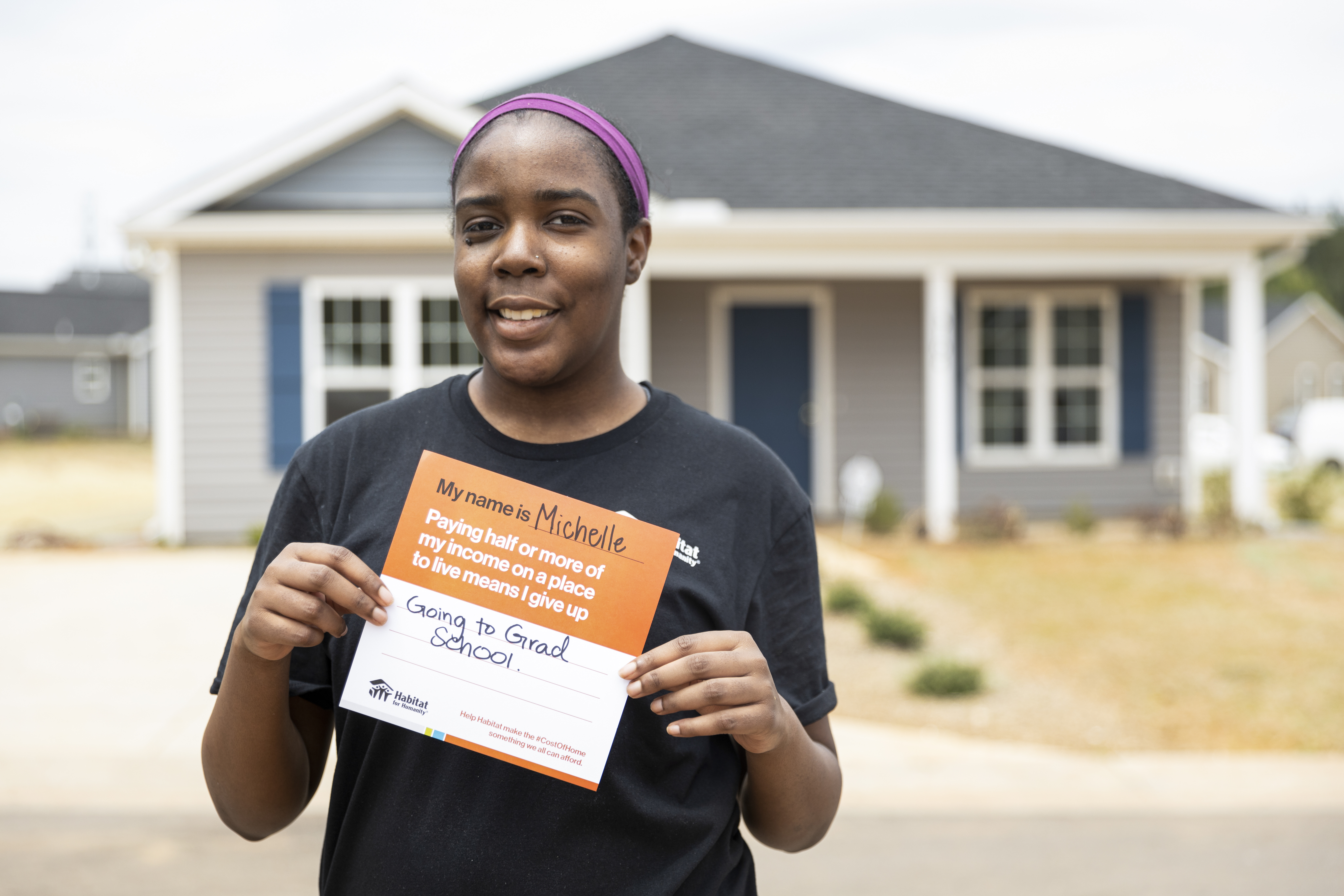 woman holding cost of home card in front of house