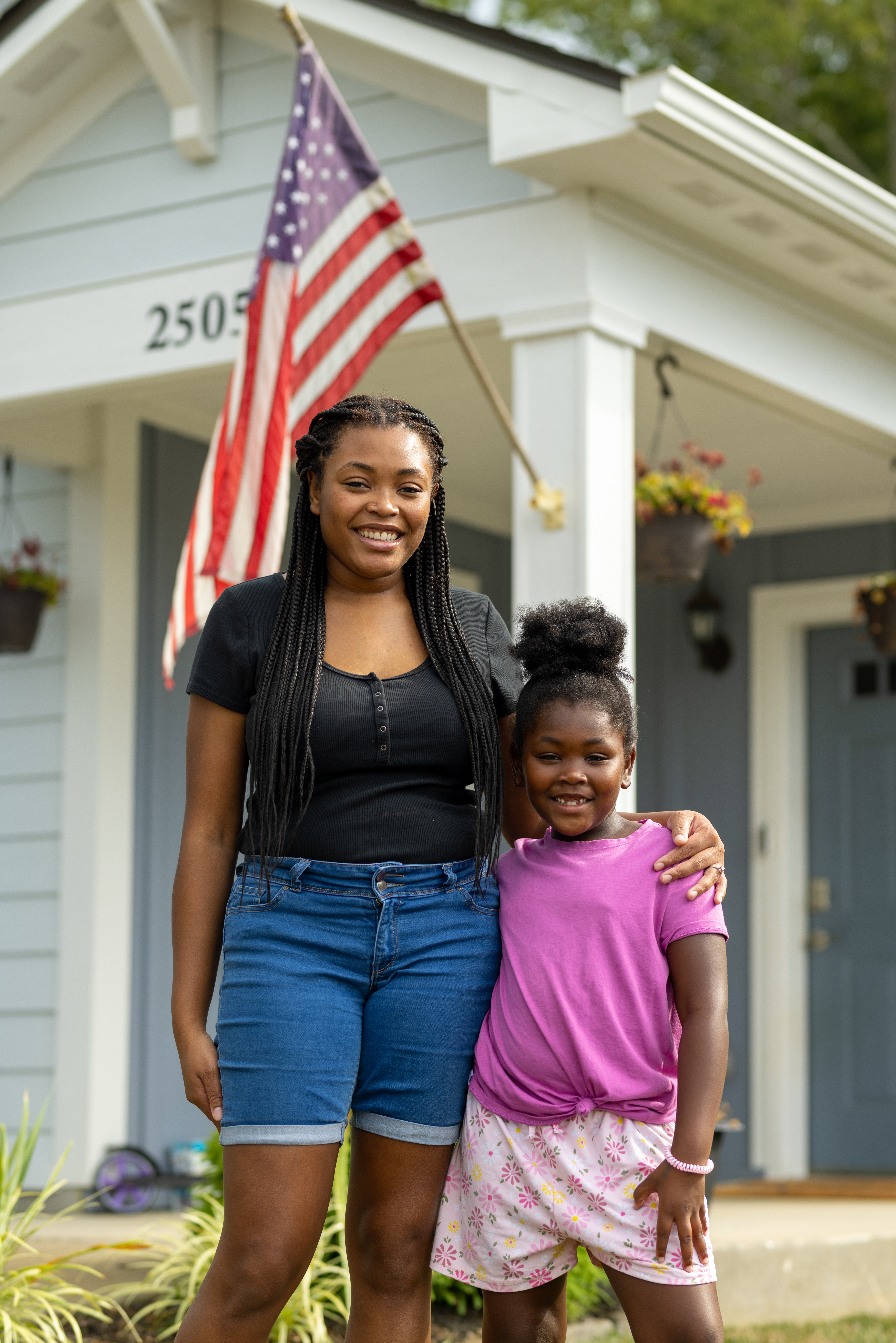 mom and daughter standing in front of their house with an american flag