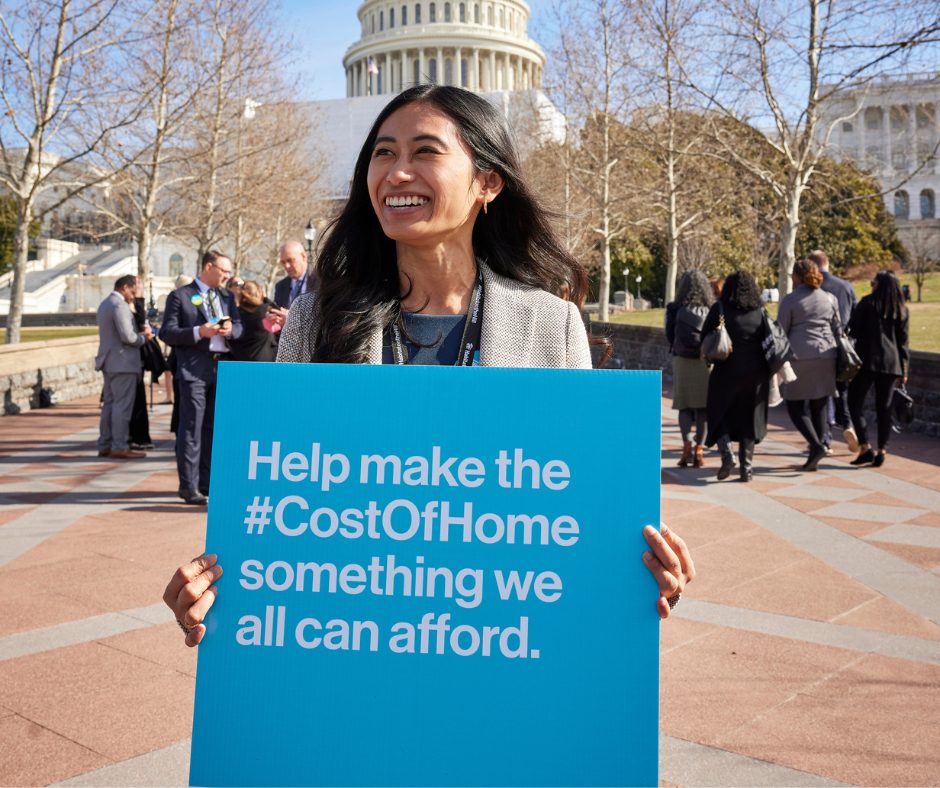 Woman holding a cost of home sign in front of the capital